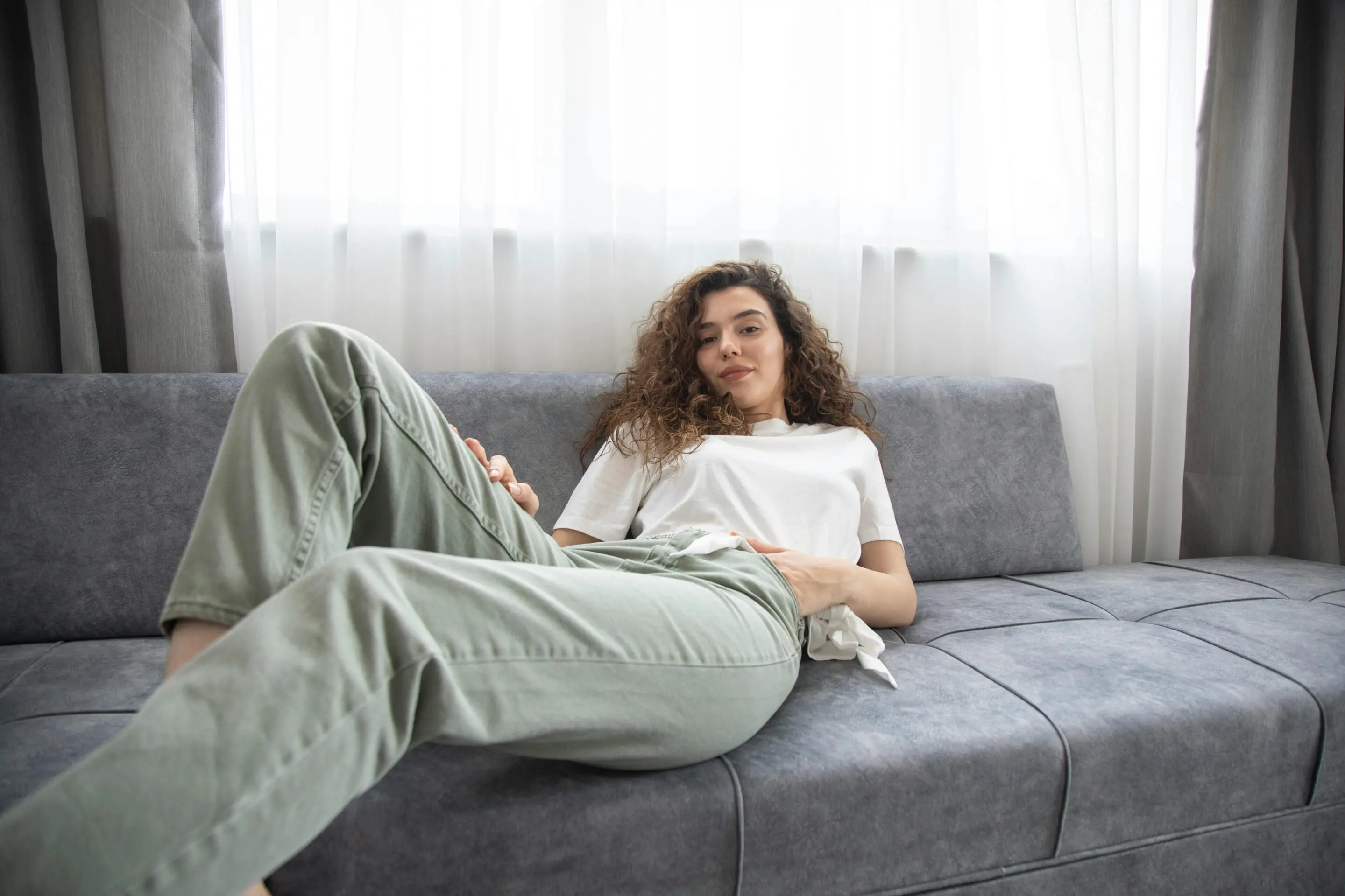 Femme détente sur canapé gris, intérieur lumineux